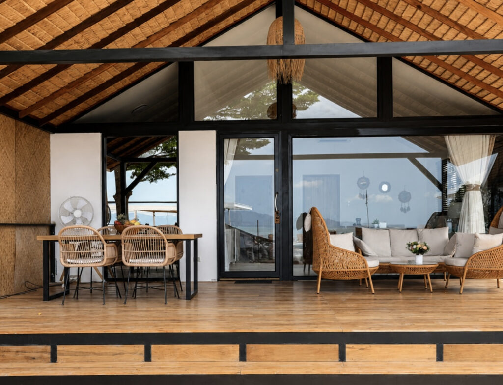 Wide villa facade with a pitched roof, wooden terrace, dining and lounge seating.