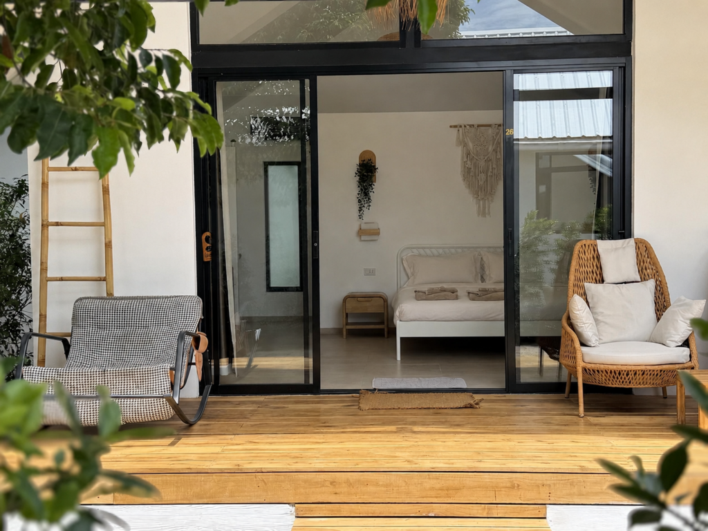 Glass-fronted villa with a wooden terrace, rocking chair and woven lounge chair.