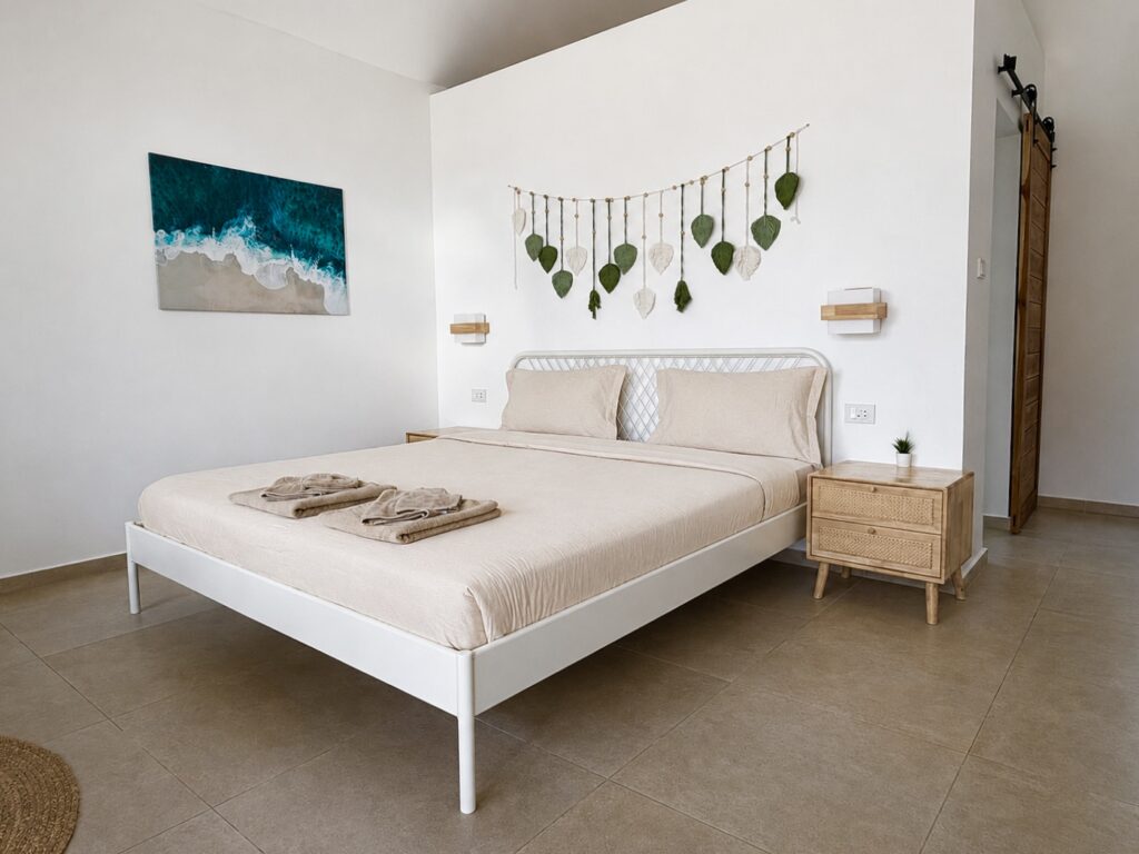 Double bed, leaf wall decor and coastal artwork beside a wooden sliding door.