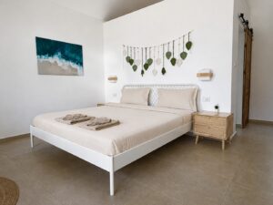 Double bed, leaf wall decor and coastal artwork beside a wooden sliding door.