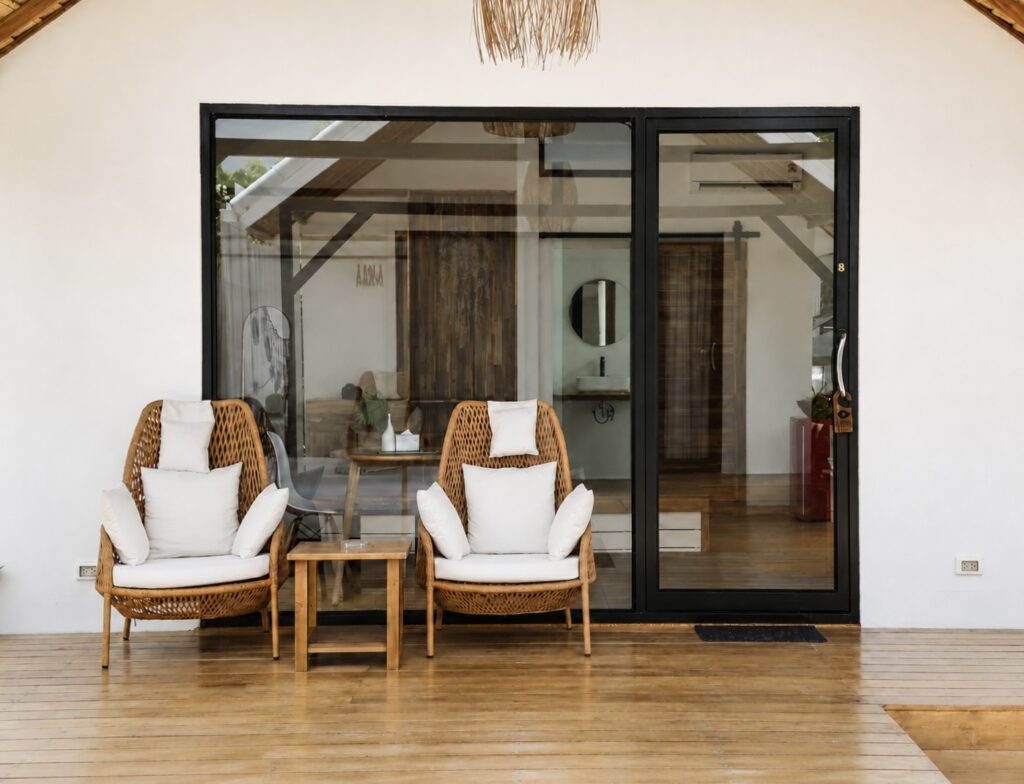 Front view of the villa with glass doors, woven chairs and a wooden terrace.