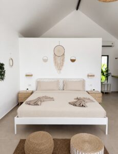 Double bed with folded towels, woven pouffes and wall decor beneath the pitched ceiling.