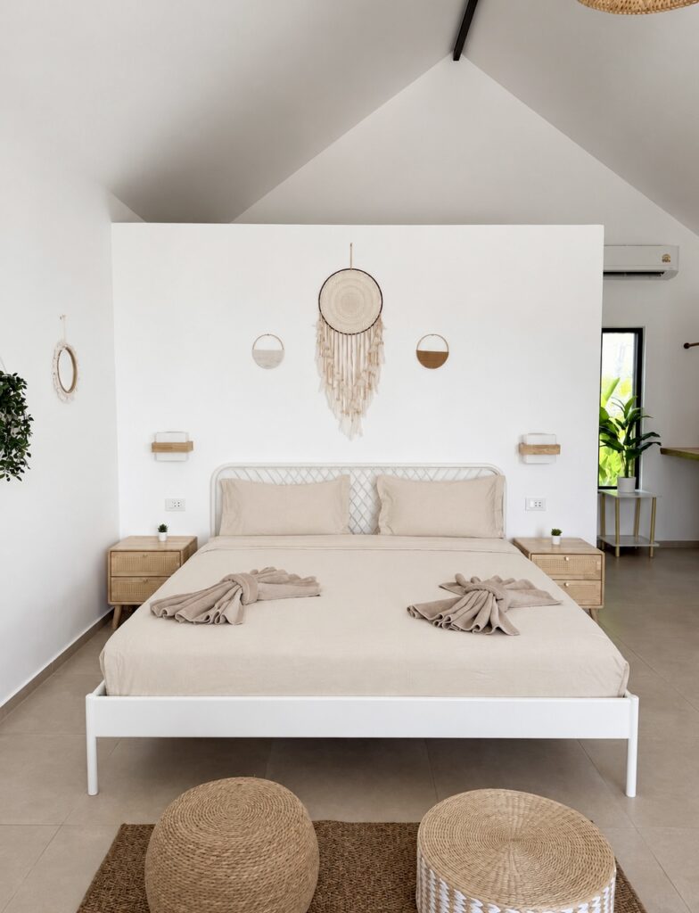 Double bed with folded towels, woven pouffes and wall decor beneath the pitched ceiling.