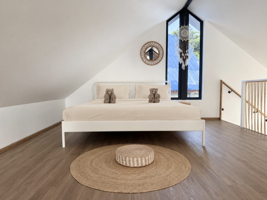 Wide view of the loft bed, sloping roof, triangular window and round woven rug.
