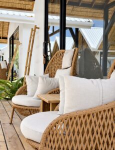 Woven outdoor chairs and white cushions beside the glass facade.