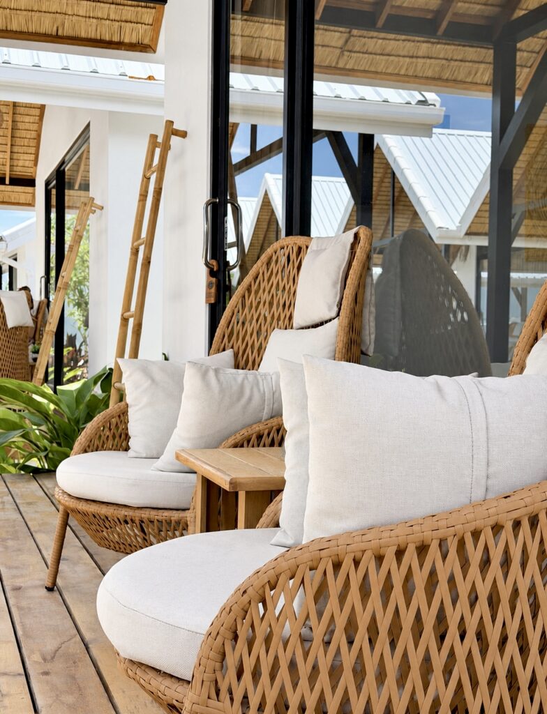 Woven outdoor chairs and white cushions beside the glass facade.
