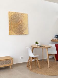 Dining table and white chairs beside a refreshment shelf and red mini refrigerator.
