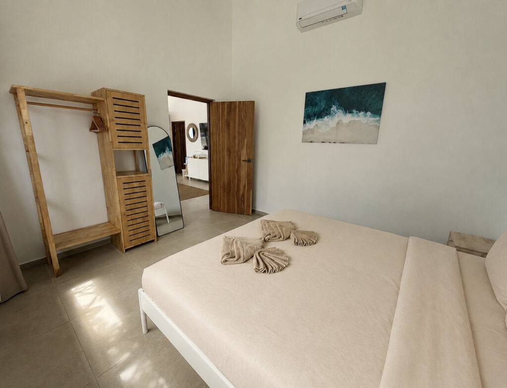 Bedroom with a double bed, wooden wardrobe, wall mirror and coastal artwork.