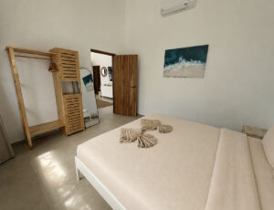 Bedroom with a double bed, wooden wardrobe, wall mirror and coastal artwork.