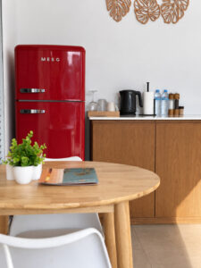 Red refrigerator and wooden kitchen cabinetry beside the dining table.