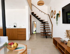 Living room with a wooden staircase, kitchen area and a fruit bowl on the coffee table.