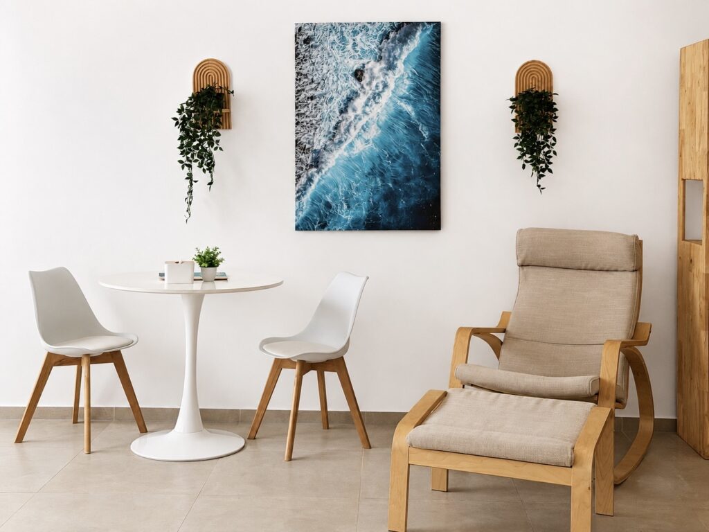 White dining table, two chairs and a cushioned armchair beneath coastal wall art.