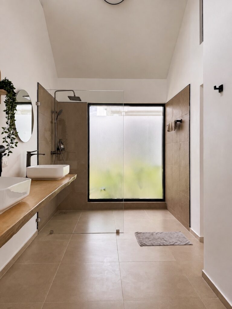 Bathroom vanity and shower beside a tall frosted window.