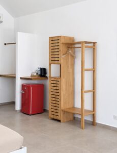Wooden clothes rack and refreshment corner with a red mini refrigerator and kettle.