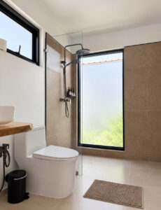 Bathroom with a toilet and shower beside a tall frosted window.