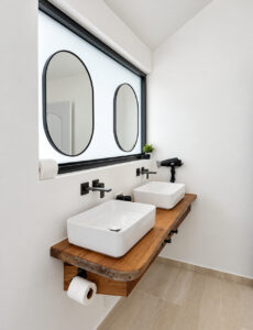 Long wooden bathroom vanity with twin basins and oval mirrors.