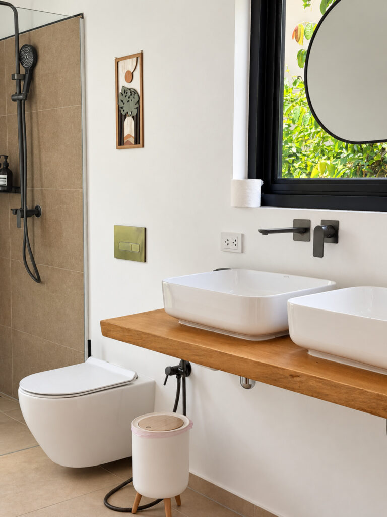 Bathroom with countertop basins, a round mirror, toilet and shower.