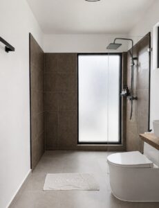 Bathroom with an overhead shower, glass screen, toilet and frosted window.