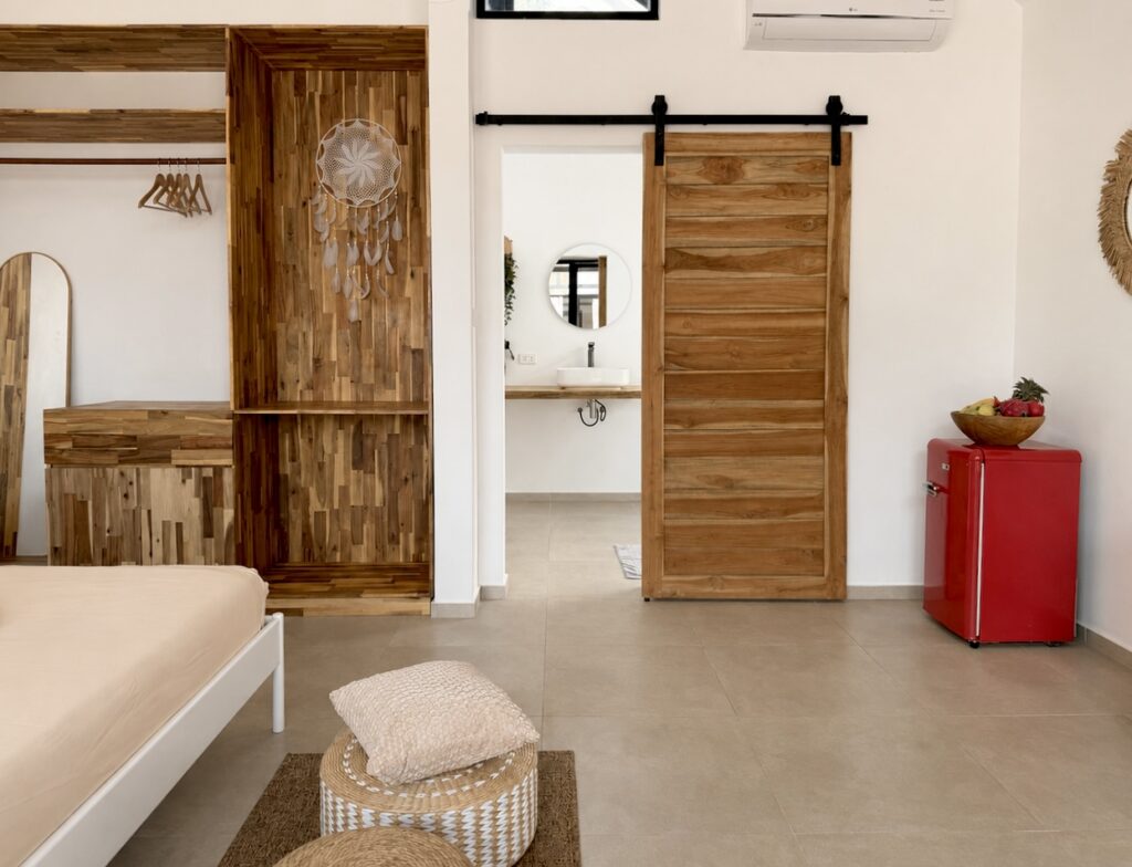 Bedroom view with a wooden wardrobe, sliding bathroom door and red mini refrigerator.