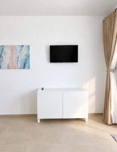 Wall-mounted television and coastal artwork above a white sideboard.