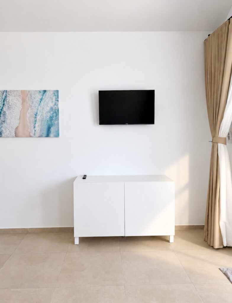 Wall-mounted television and coastal artwork above a white sideboard.
