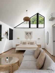Open room with a double bed, sofa, coffee table and high triangular glazing.