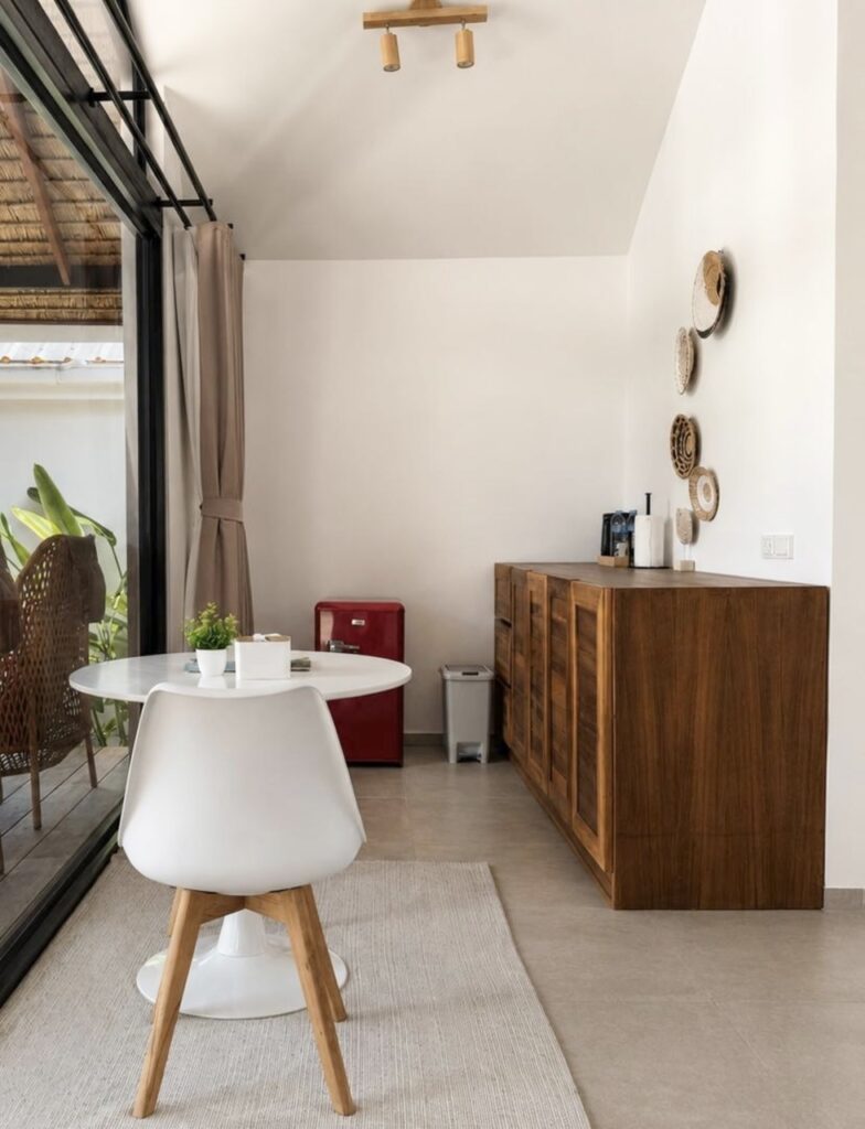Dining table, woven chair, wooden refreshment sideboard and red mini refrigerator.