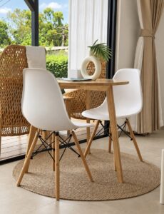 Wooden dining table with white and woven chairs on a round rug beside the glass doors.