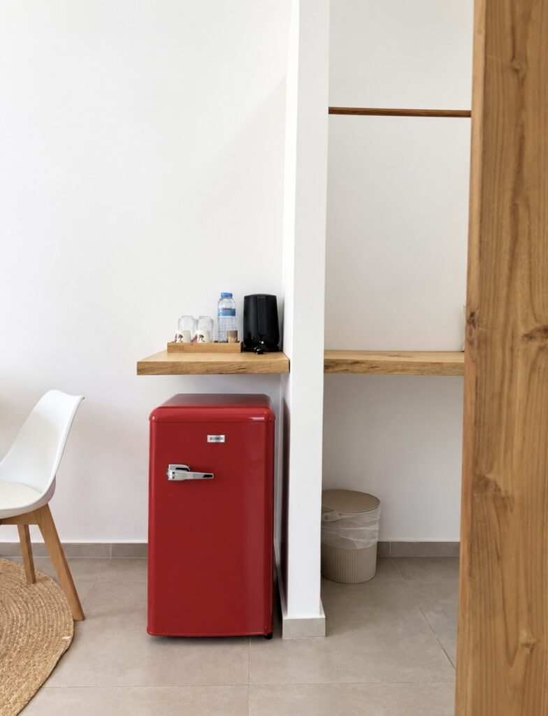 Open wooden wardrobe beside a red mini refrigerator and refreshment shelf.