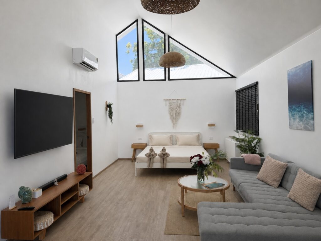 Wide view of the double bed, grey sofa, television and high triangular glazing.