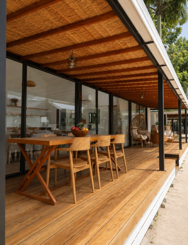 Long covered wooden terrace with dining and lounge seating beside the glass facade.