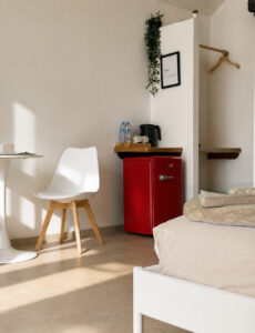 Red mini refrigerator, kettle and dining table beside the bed.