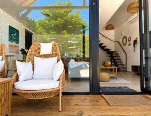 Woven terrace chair with white cushions beside the glass entrance doors.