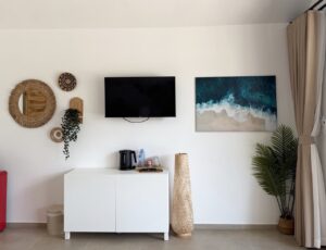 Television and coastal wall art above a white sideboard with an electric kettle and cups.