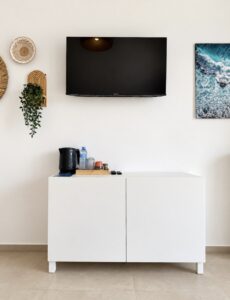 Television and coastal artwork above a white cabinet with an electric kettle and cups.