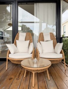 Two high-backed woven lounge chairs with white cushions and a round table.