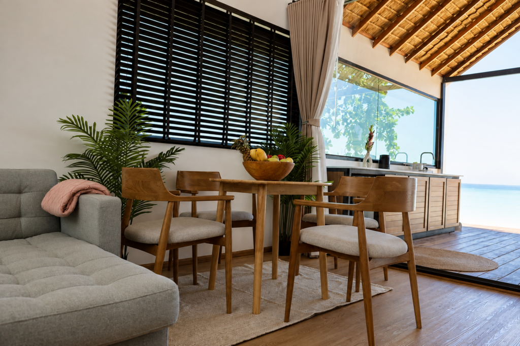 Indoor dining table and sofa beside open doors with a sea outlook.