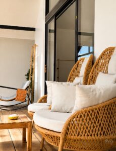 High-backed woven lounge chair with white cushions beside the glass facade.