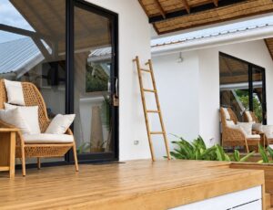 Wooden terrace, woven chair and decorative ladder beside the glass entrance.