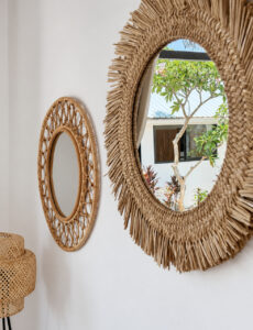 Round woven-framed mirrors reflecting greenery outside the villa.