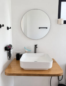 White countertop basin, black tap and round bathroom mirror.