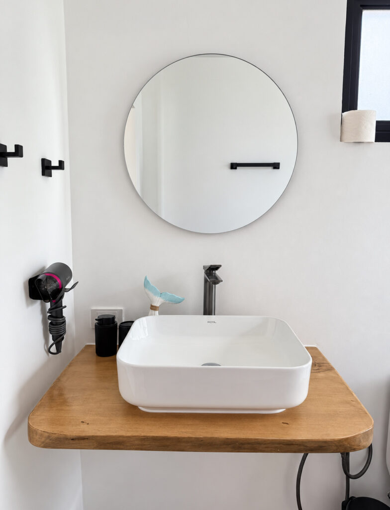 White countertop basin, black tap and round bathroom mirror.
