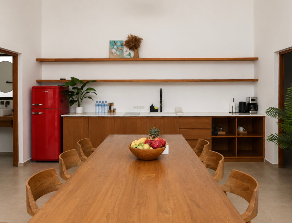 Dining table with a fruit bowl facing wooden kitchen cabinets and a red refrigerator.