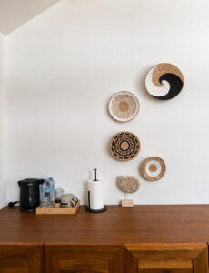 Wooden sideboard with kettle and drinking water beneath round woven wall decor.