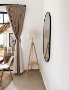 Tall wall mirror and tripod floor lamp beside the curtains.