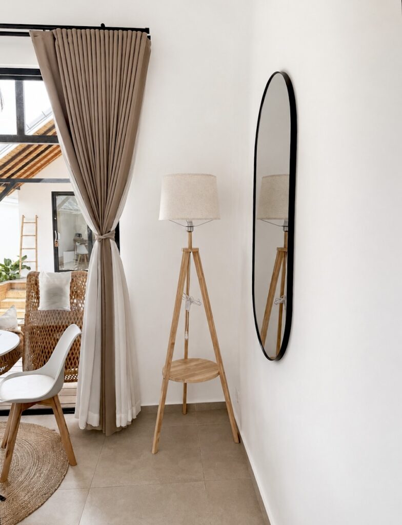 Tall wall mirror and tripod floor lamp beside the curtains.