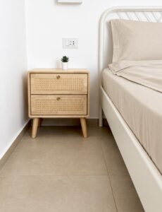 Wooden bedside table with a small plant beside the double bed.