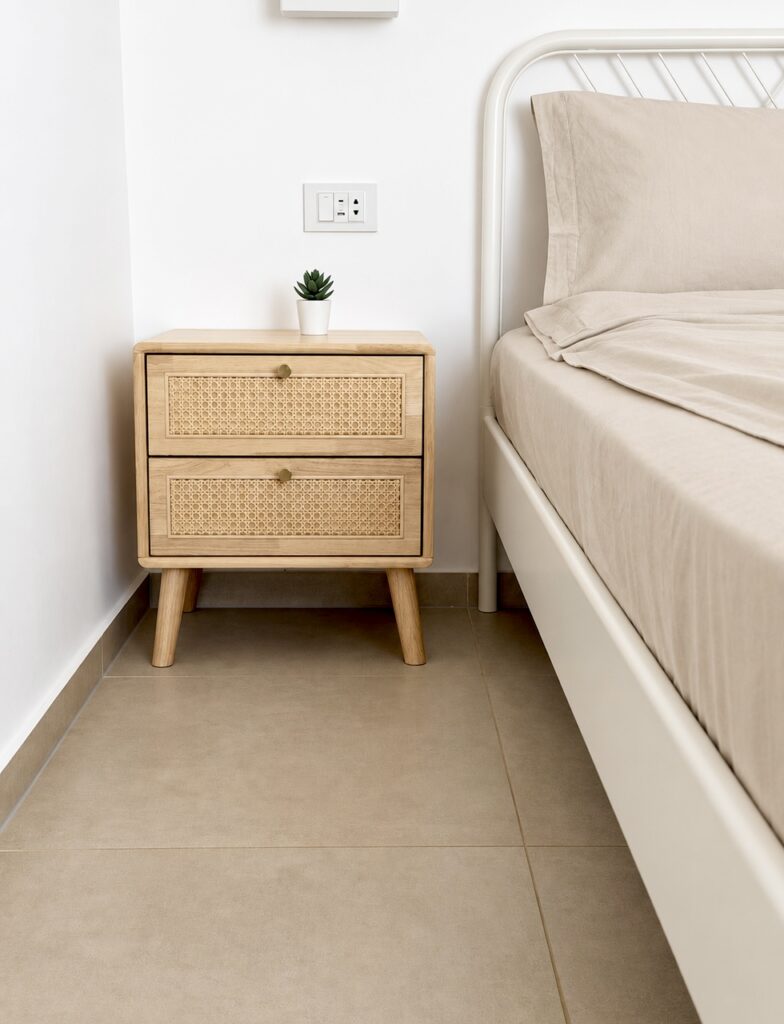 Wooden bedside table with a small plant beside the double bed.