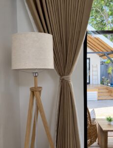 Tripod floor lamp beside tied curtains and the glass doors.