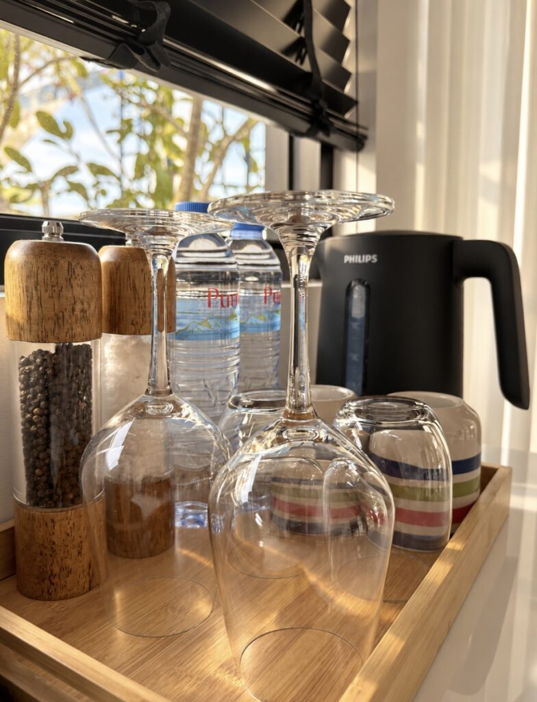 Electric kettle, glasses and bottled drinking water on a wooden kitchen tray.